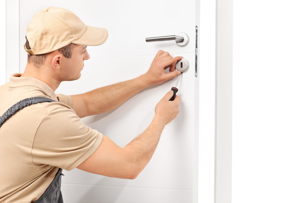 young male locksmith installing a lock in a door